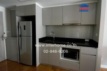 Modern kitchen with grey cabinets, stainless steel refrigerator, built-in microwave and black countertop