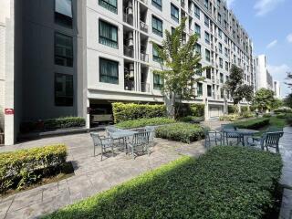 Exterior view of a multi-story residential building with outdoor seating area and greenery