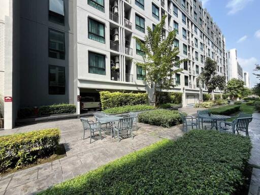 Exterior view of a multi-story residential building with outdoor seating area and greenery