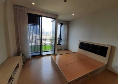 Bedroom with large window and balcony access, partially furnished with bed frame and drawers