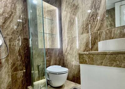 Modern bathroom with glass shower partition and marble walls