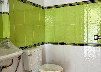 Bathroom featuring white and green tiles with a sink and toilet.