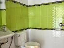 Bathroom featuring white and green tiles with a sink and toilet.