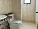 A bathroom with tiled walls, a window, a sink with vanity, and a toilet.