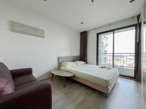 Modern bedroom with a double bed, purple armchair, small round table, balcony, and large window