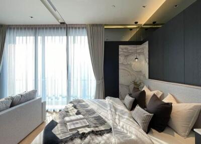Modern bedroom with large windows, elegant curtains, a comfortable bed, and a seating area.