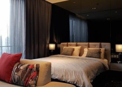Modern bedroom with a large bed, upholstered headboard, bedside lamps, and large windows with curtains.
