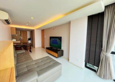 Modern living room with a wall-mounted TV, sectional sofa, and an open view into the kitchen area