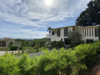 Modern two-story house with surrounding greenery and a distant view of the sea