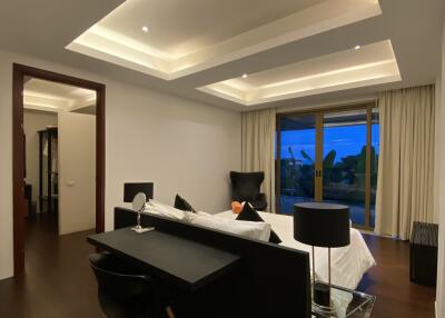 Modern bedroom with dark wood flooring, an elegant bed, a desk, and large windows.