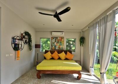 A bright bedroom with a bed, ceiling fan, and large windows.