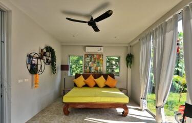 A bright bedroom with a bed, ceiling fan, and large windows.