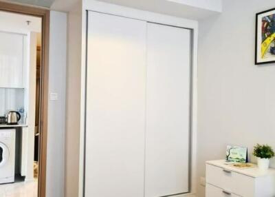 Modern bedroom with white sliding door closet, dresser, and view into kitchen area