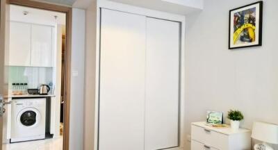 Modern bedroom with white sliding door closet, dresser, and view into kitchen area