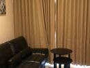 Simple living room with black leather sofa and curtains