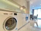 Modern kitchen with integrated appliances including washing machine and built-in oven, leading to dining area