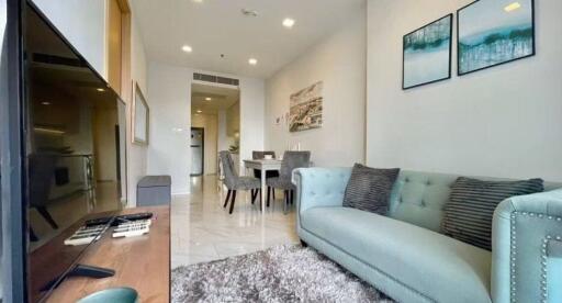 Modern living room with a comfortable sofa, wall art, and a view towards the dining area and kitchen