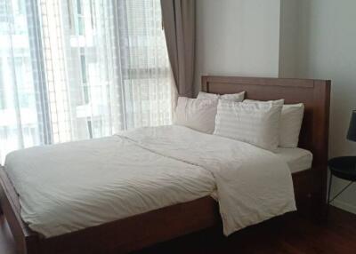 Cozy bedroom with wooden bed frame, white linens, sheer curtains, and black bedside lamp