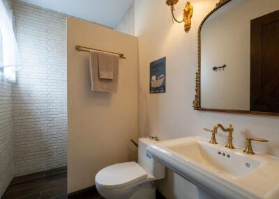 Bathroom with white sink and toilet, featuring gold fixtures and a wall-mounted mirror