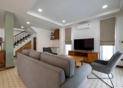 Modern living room with a grey couch, flat-screen TV, and staircase