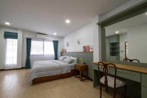 Spacious bedroom with bed, side table, large windows, and a vanity desk