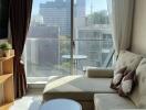 Cozy living room with a sofa, table, shelves, and large windows with city view.