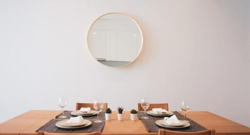 Dining room with a wooden table set for four, wall mirror, and small plants