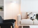 Modern living room with light-colored sofa and decorative pillows, black accent chair, bookshelf, and potted plant.