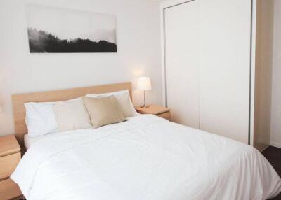 Spacious bedroom with a minimalist design, featuring a double bed, wooden side tables, and a large wardrobe.