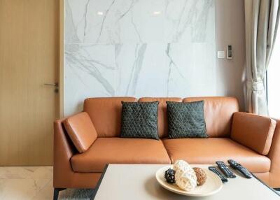 Modern living room with a brown leather sofa, marble wall, and natural light