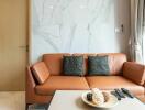 Modern living room with a brown leather sofa, marble wall, and natural light