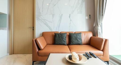 Modern living room with a brown leather sofa, marble wall, and natural light