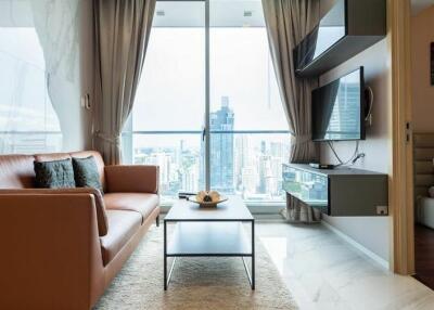 Modern living room with a glass window overlooking a cityscape, furnished with a brown sofa, coffee table, and wall-mounted TV