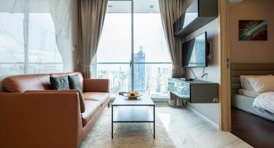 Modern living room with a city view, featuring a brown leather couch, wall-mounted TV, and a small coffee table.