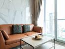 Modern living room with a brown leather sofa, coffee table, and large window.