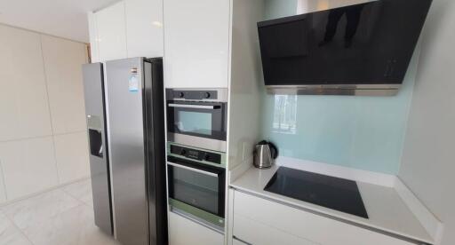 Modern kitchen with stainless steel refrigerator, built-in ovens, electric cooktop and black range hood