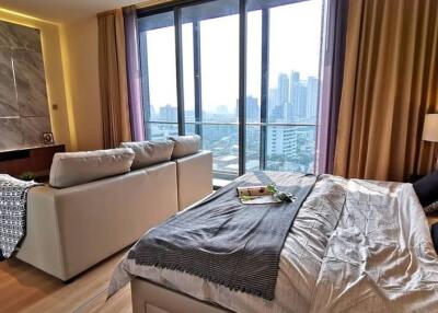 Modern bedroom with bed, sofa, large windows, and city view