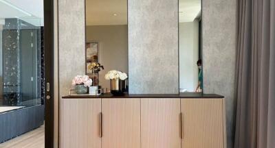 A bedroom with a wooden cabinet, decorative flowers, and mirrored panels