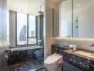 Modern bathroom with city view, featuring a bathtub, toilet, and sink with a marble countertop