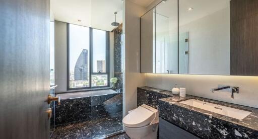 Modern bathroom with city view, featuring a bathtub, toilet, and sink with a marble countertop