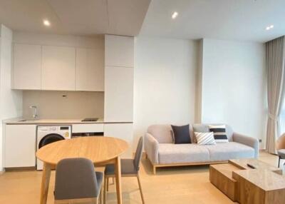 Modern living room with an integrated kitchenette, featuring a sofa, coffee table, dining table, chair and large windows with curtains.