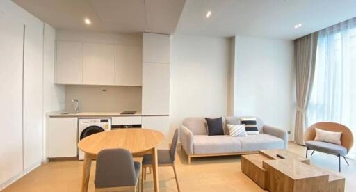 Modern living room with an integrated kitchenette, featuring a sofa, coffee table, dining table, chair and large windows with curtains.