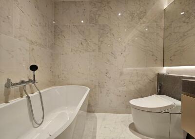 Modern bathroom with marble tiles, bathtub, and wall-mounted toilet