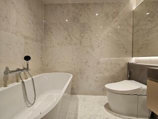 Modern bathroom with marble tiles, bathtub, and wall-mounted toilet