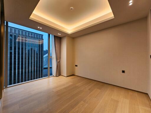 Empty modern living area with a large window, wooden flooring, and recessed lighting