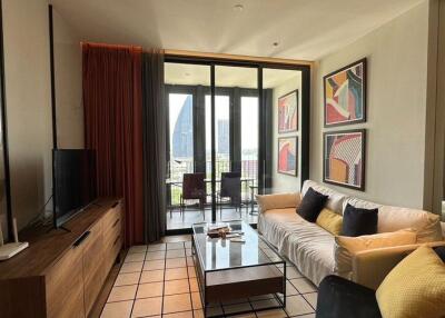 Modern living room with a cozy seating area, TV and decor, leading to a balcony with an outdoor view.