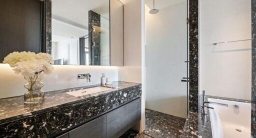 Modern bathroom with black and white marbled decor, lighted mirror, and glass-enclosed shower area