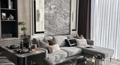 Modern living room with gray sectional sofa, marble accent wall, large window with sheer curtains, and dining table