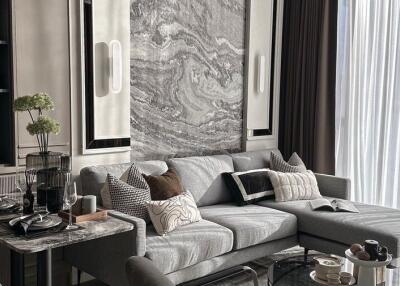 Modern living room with gray sofa, marble accents, dining area, and large window with sheer curtains
