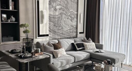 Modern living room with gray sofa, marble accents, dining area, and large window with sheer curtains